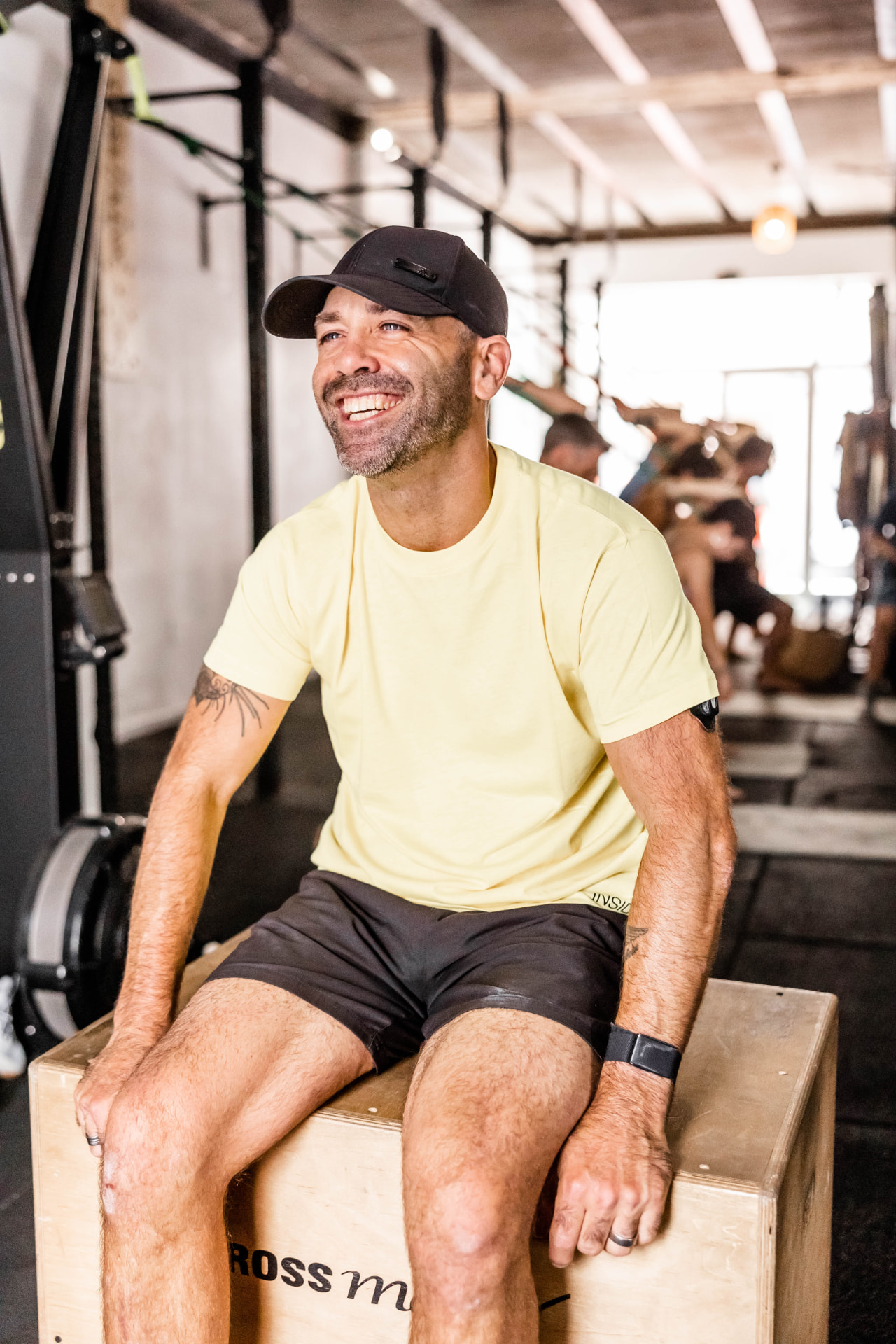 Brett smiling and laughing while sitting on a wooden gym box between workouts.